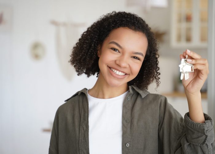 Face of young african american girl which is holding key from new apartment. Carefree teenager is smiling. Happy home owner is relocating. Mortgage loan and real estate purchase conceptual image.